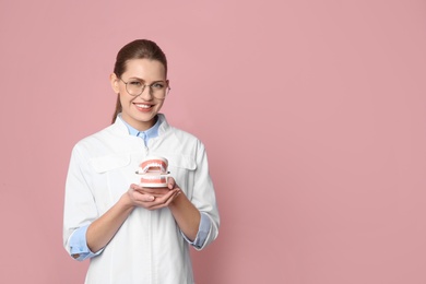 Photo of Female dentist holding jaws model on color background. Space for text