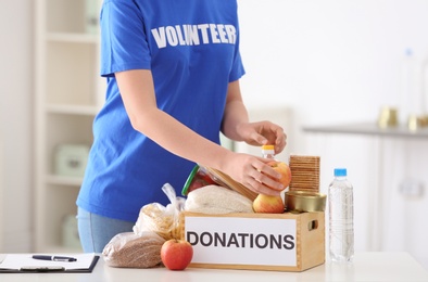 Photo of Female volunteer putting food products in donation box indoors