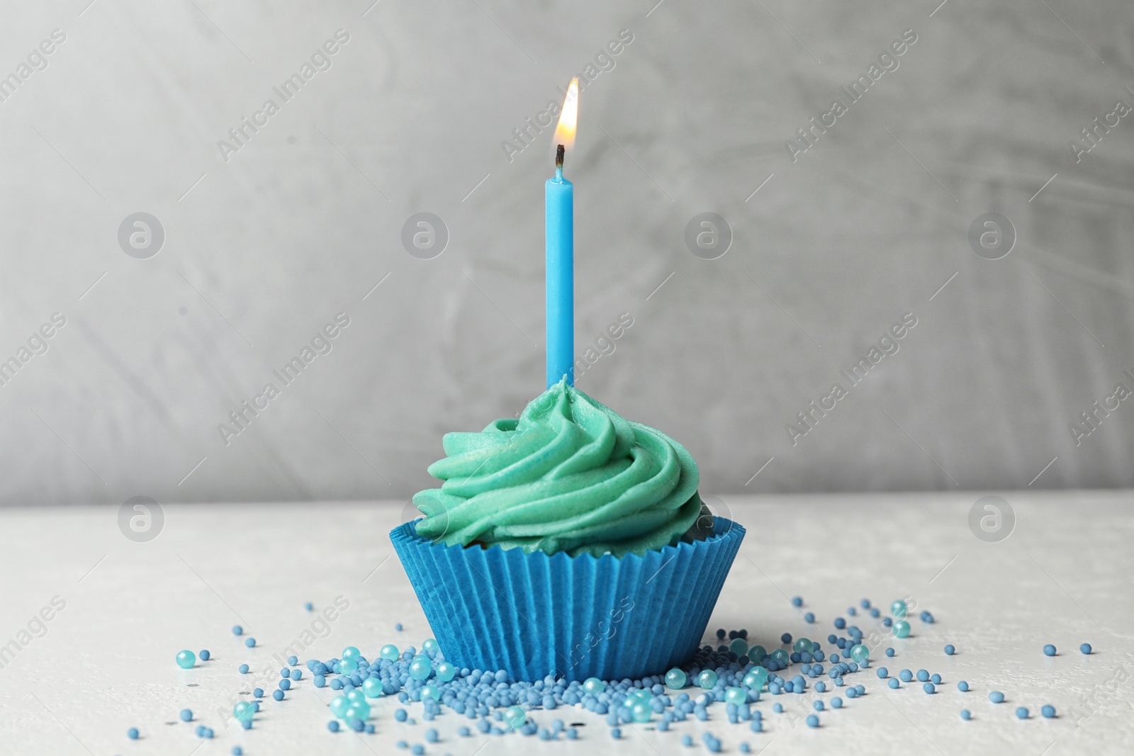 Photo of Delicious birthday cupcake with cream and burning candle on table