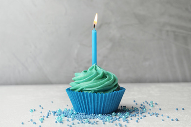 Delicious birthday cupcake with cream and burning candle on table