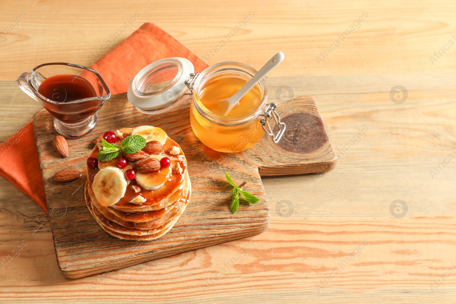 Photo of Stack of tasty pancakes with banana, berries, nuts and syrup on wooden table