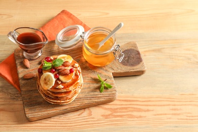 Photo of Stack of tasty pancakes with banana, berries, nuts and syrup on wooden table