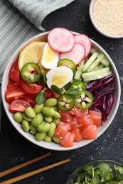 Photo of Poke bowl with salmon, edamame beans and vegetables on black table, flat lay