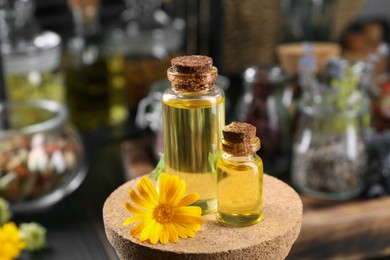 Photo of Bottles with herbal essential oils and calendula flower on blurred background