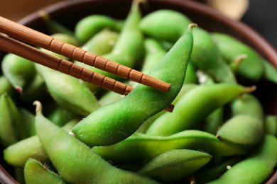 Photo of Bowl with green edamame beans in pods and chopsticks, closeup