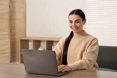 Photo of Happy woman working with laptop at wooden desk in room