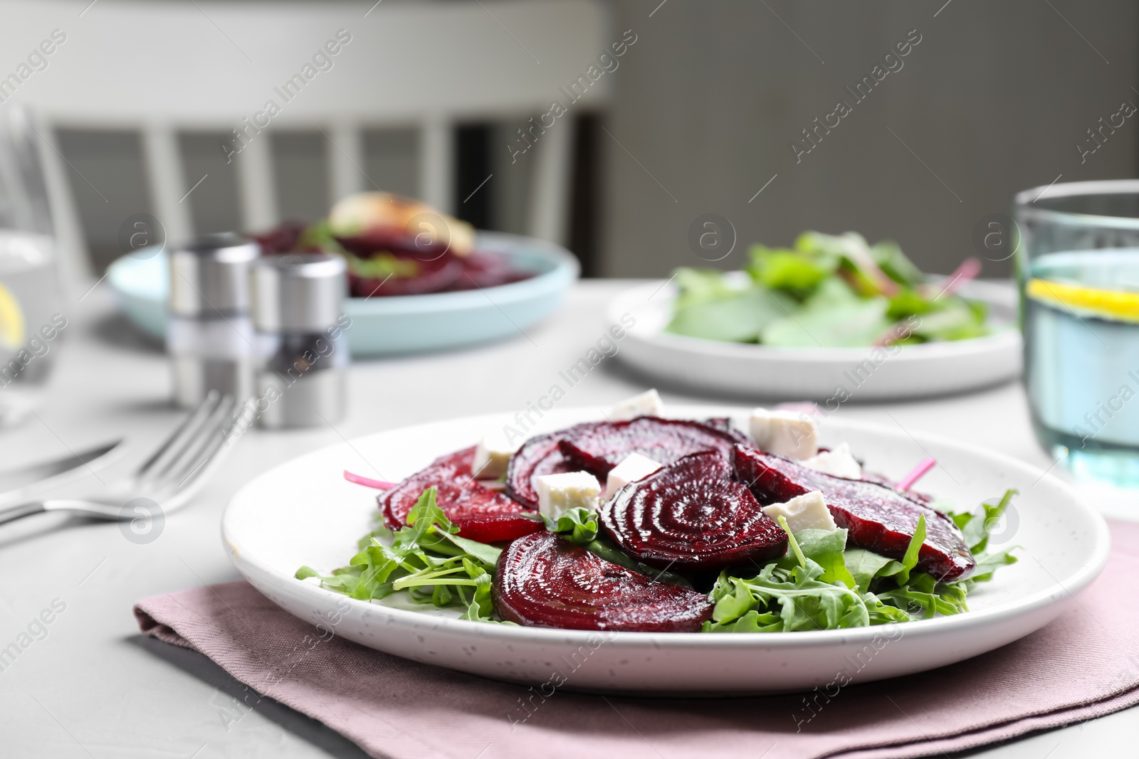 Photo of Roasted beetroot slices with feta cheese and arugula on light grey table