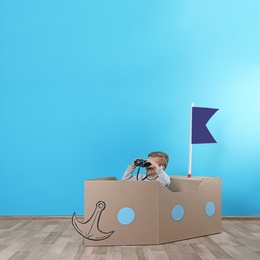 Photo of Cute little boy playing with cardboard ship near color wall. Space for text