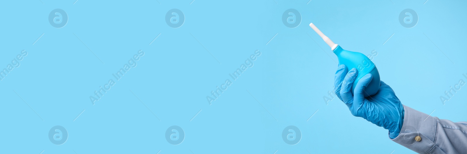 Photo of Man holding enema on light blue background, closeup