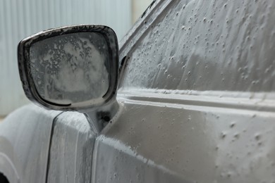 Photo of Automobile side-view mirror with cleaning foam at car wash, closeup