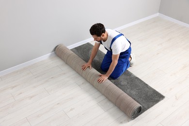 Photo of Worker unrolling new carpet on floor in room, space for text