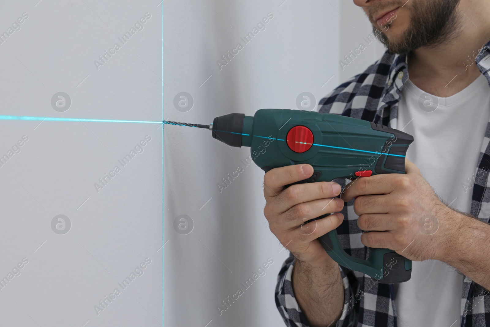 Photo of Man using cross line laser level for accurate measurement and drilling hole in light wall, closeup