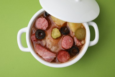 Meat solyanka soup with thin dry smoked sausages in pot on light green background, top view