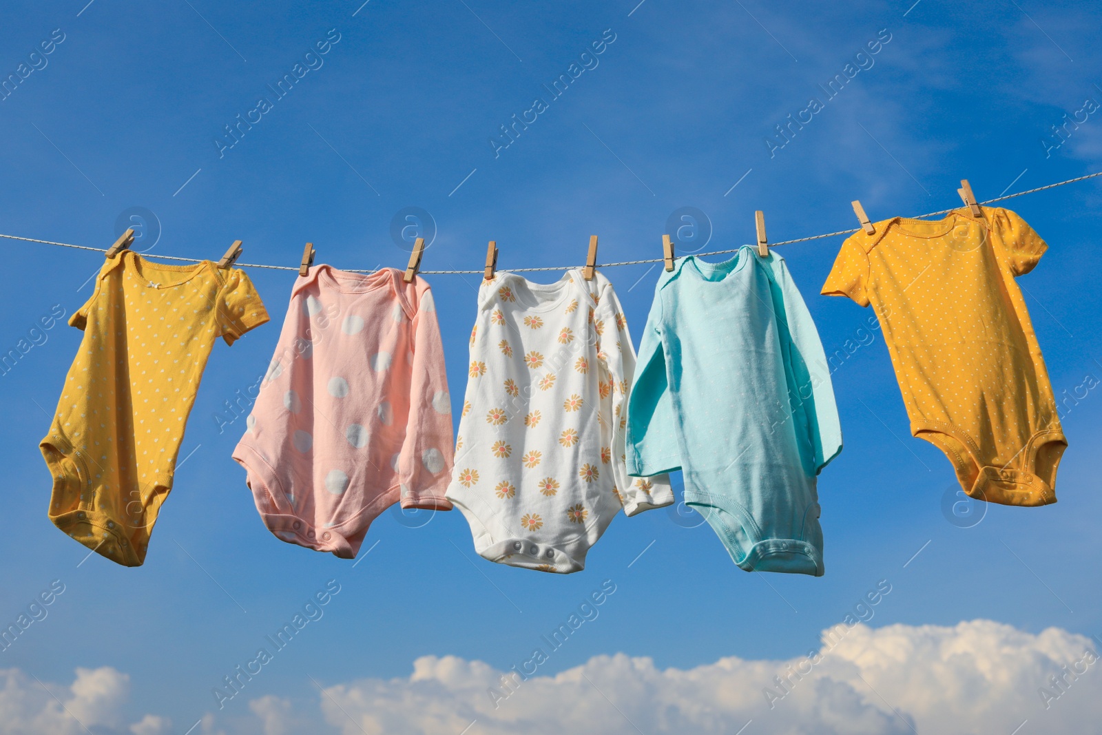 Photo of Clean baby onesies hanging on washing line against sky. Drying clothes