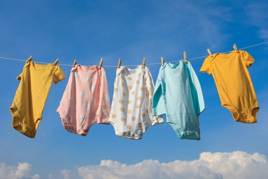 Photo of Clean baby onesies hanging on washing line against sky. Drying clothes