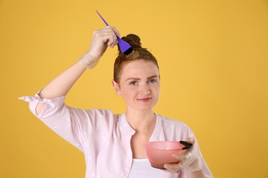 Young woman dyeing her hair with henna on yellow background