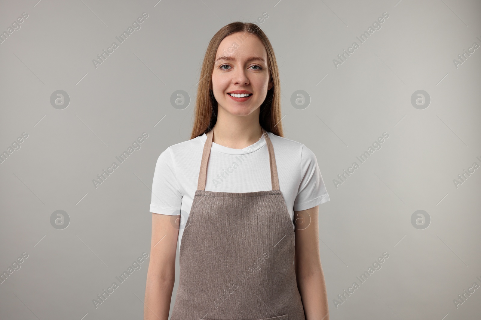 Photo of Beautiful young woman wearing kitchen apron on grey background. Mockup for design