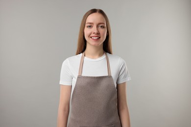 Beautiful young woman wearing kitchen apron on grey background. Mockup for design