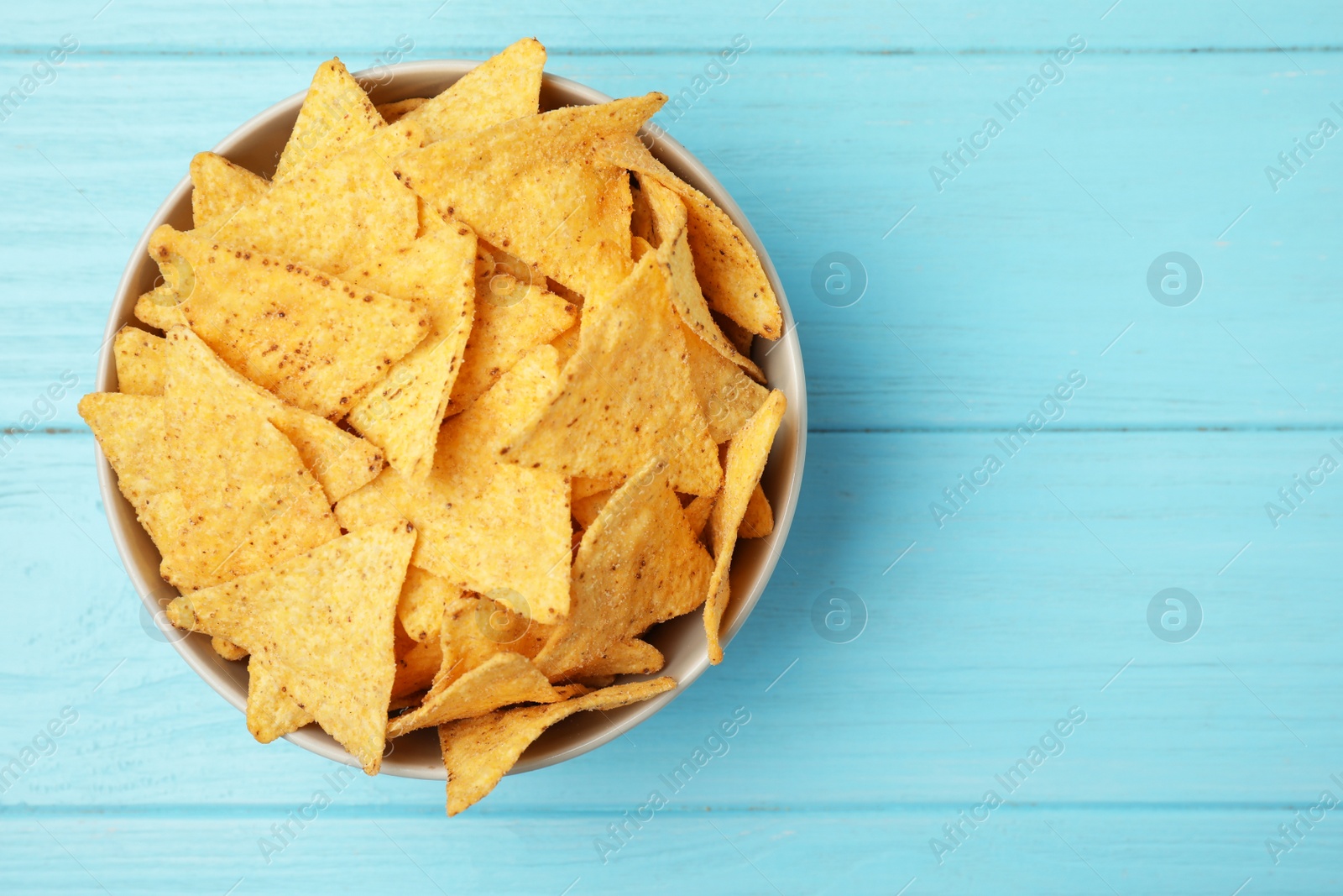 Photo of Bowl of tasty Mexican nachos chips on light blue wooden background, top view. Space for text