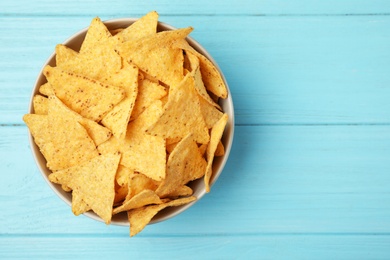 Photo of Bowl of tasty Mexican nachos chips on light blue wooden background, top view. Space for text