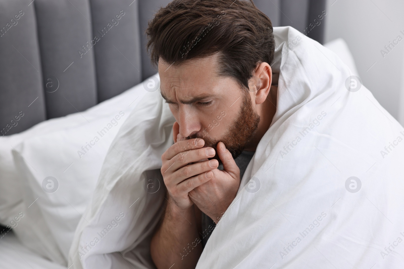 Photo of Sick man coughing on bed. Cold symptoms