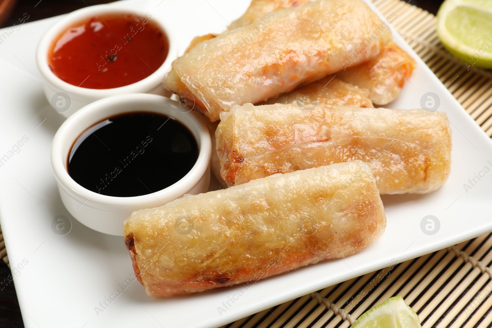 Photo of Tasty fried spring rolls and sauces on table, closeup
