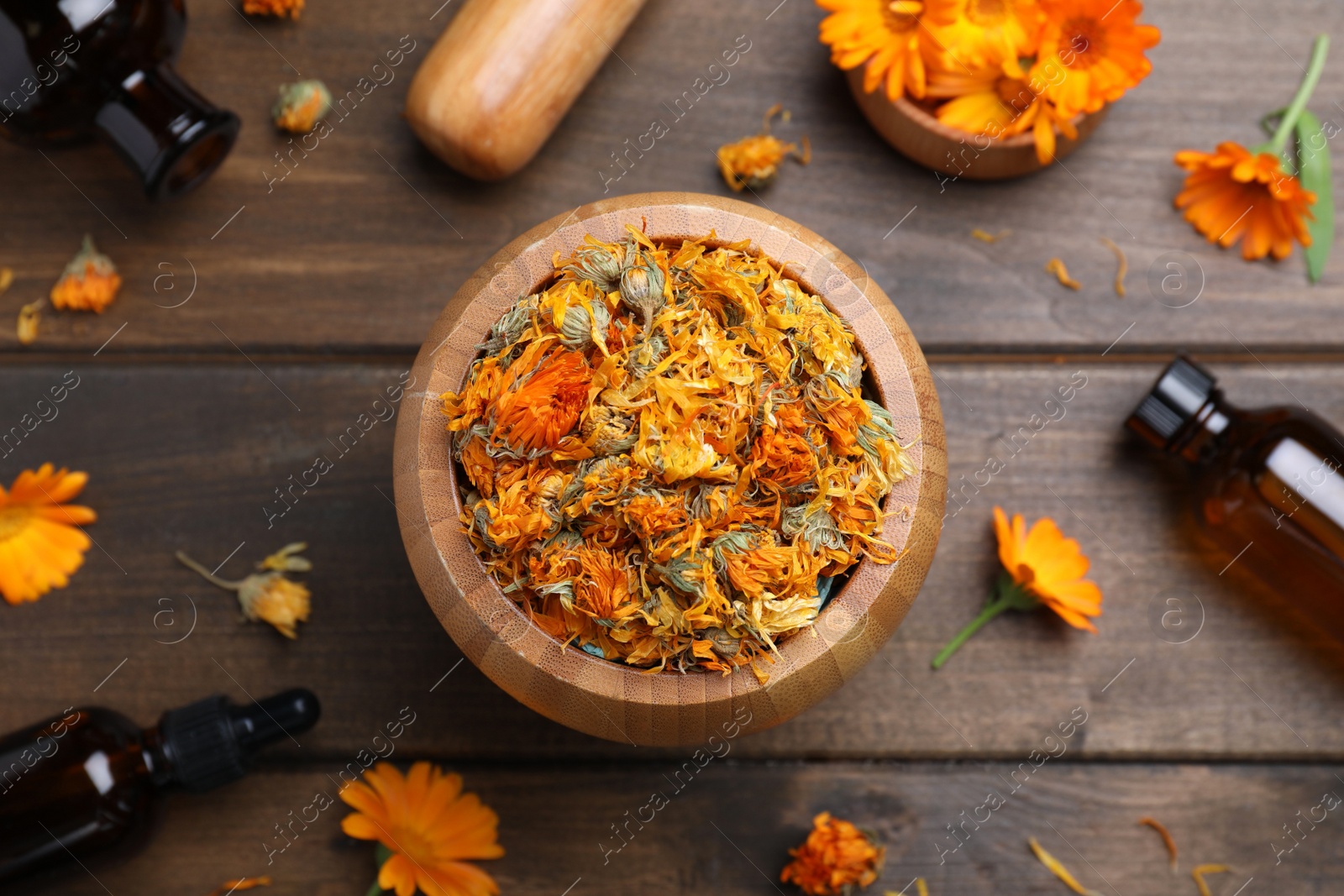 Photo of Dry calendula flowers and bottles of essential oil on wooden table, flat lay