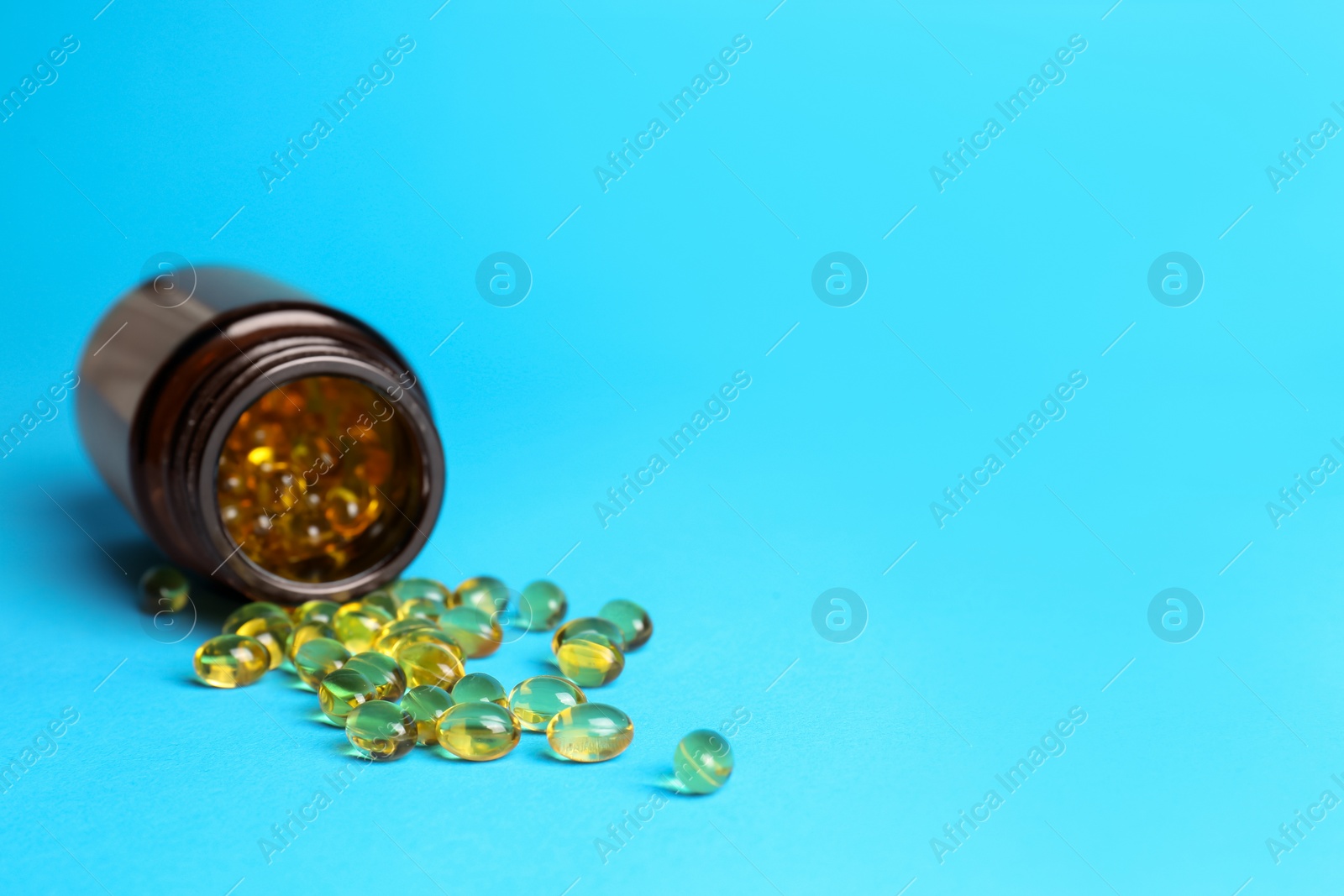 Photo of Medical bottle and yellow capsules on light blue background, space for text