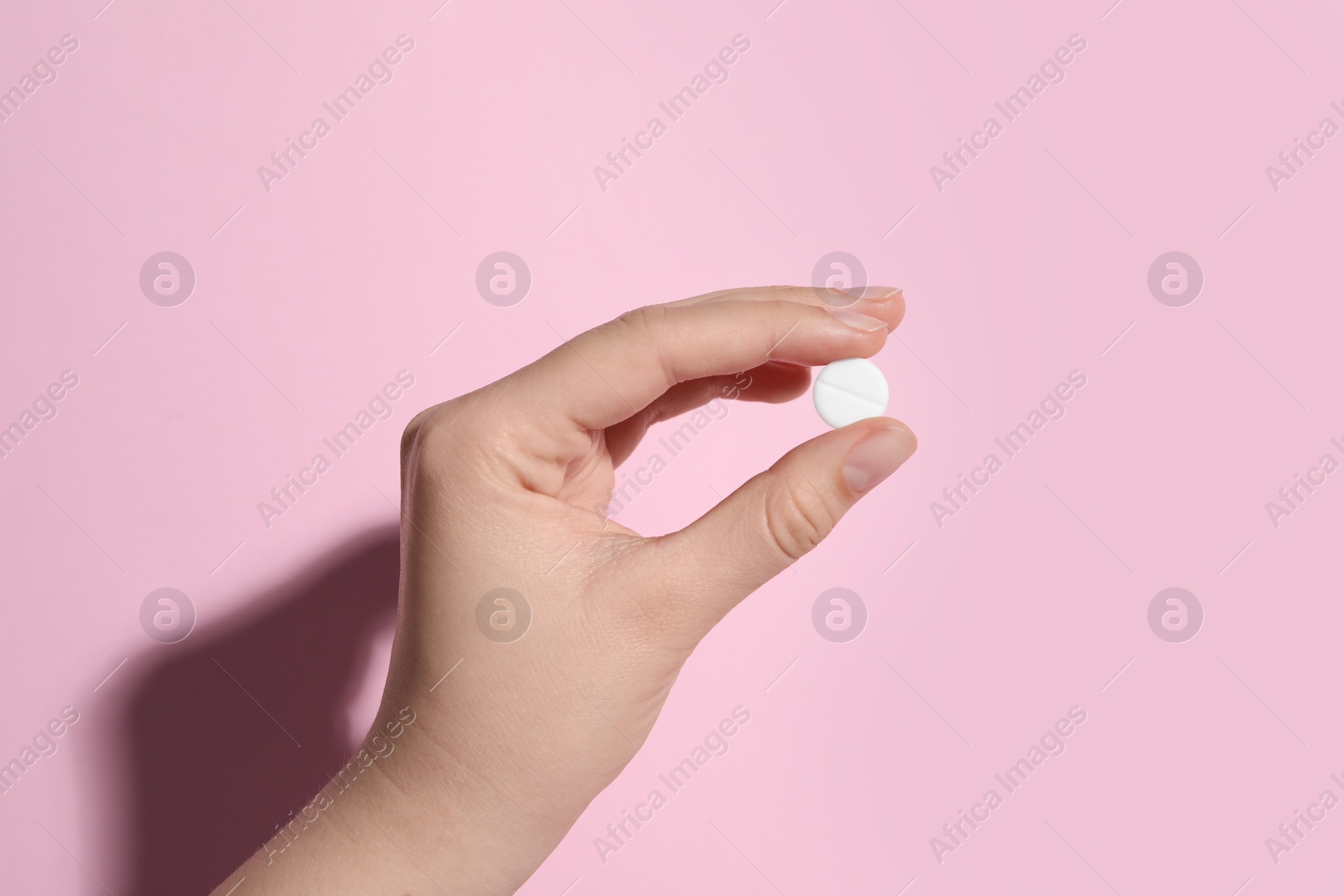 Photo of Woman holding pill on pink background, closeup