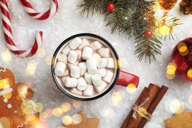 Image of Hot drink with marshmallows, sweets and festive decor on snow, flat lay