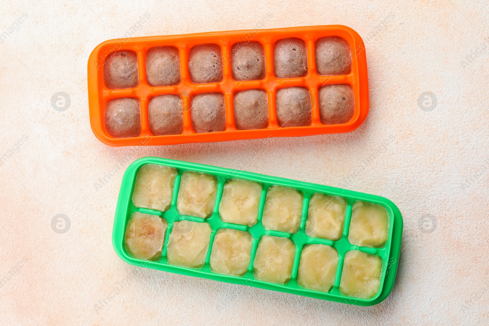 Photo of Apple and banana puree in ice cube trays on beige table, flat lay