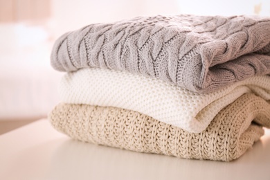 Stack of folded warm sweaters on white table indoors, closeup