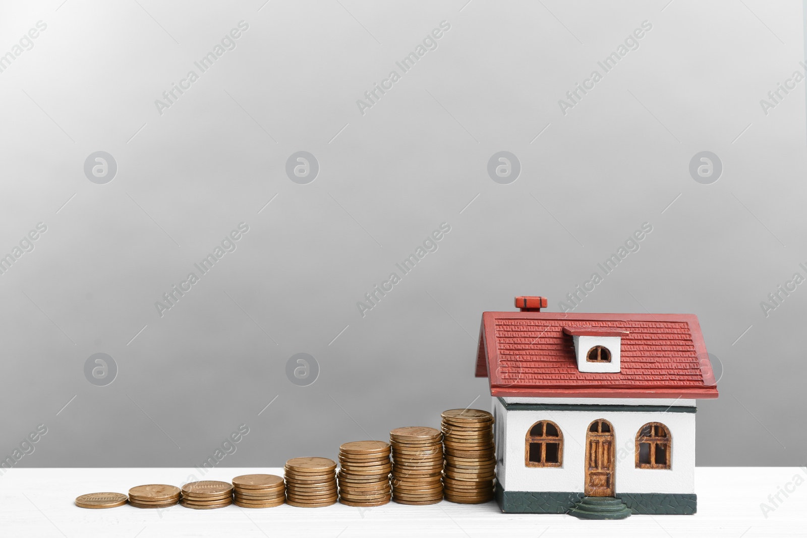 Photo of House model and coins on white wooden table against light grey background. Money savings
