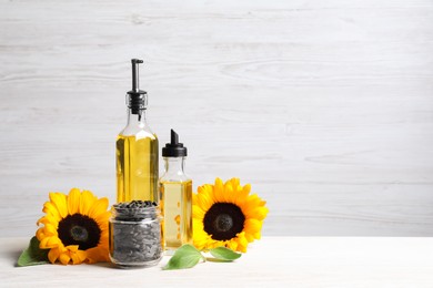 Bottles of sunflower cooking oil, seeds and yellow flowers on white wooden table, space for text