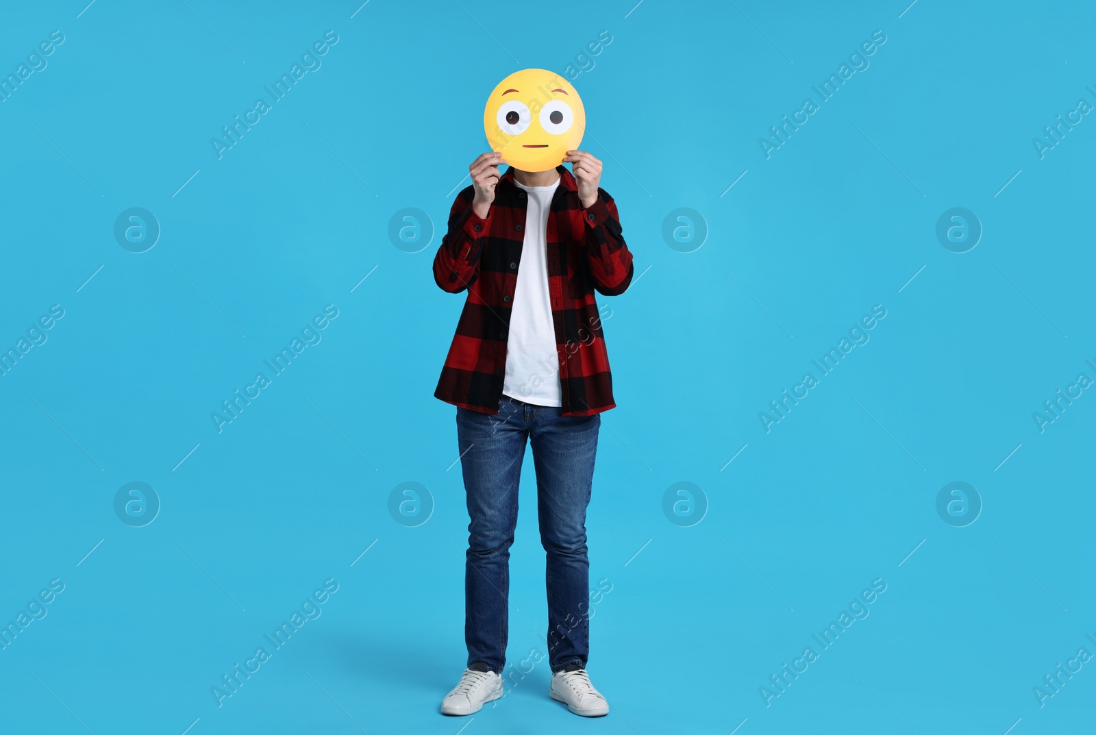 Photo of Man covering face with surprised emoticon on light blue background