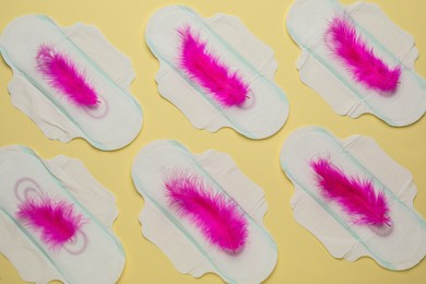 Menstrual pads with pink feathers on beige background, flat lay