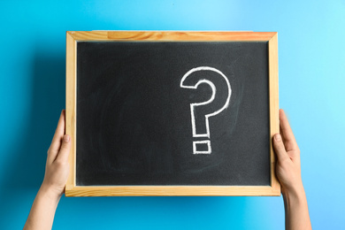 Photo of Woman holding blackboard with question mark on blue background, closeup