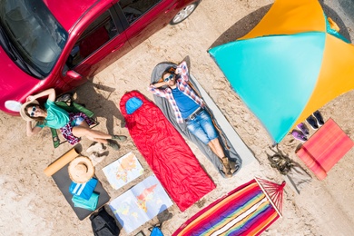 Couple with camping equipment near car on sand, aerial view. Summer trip