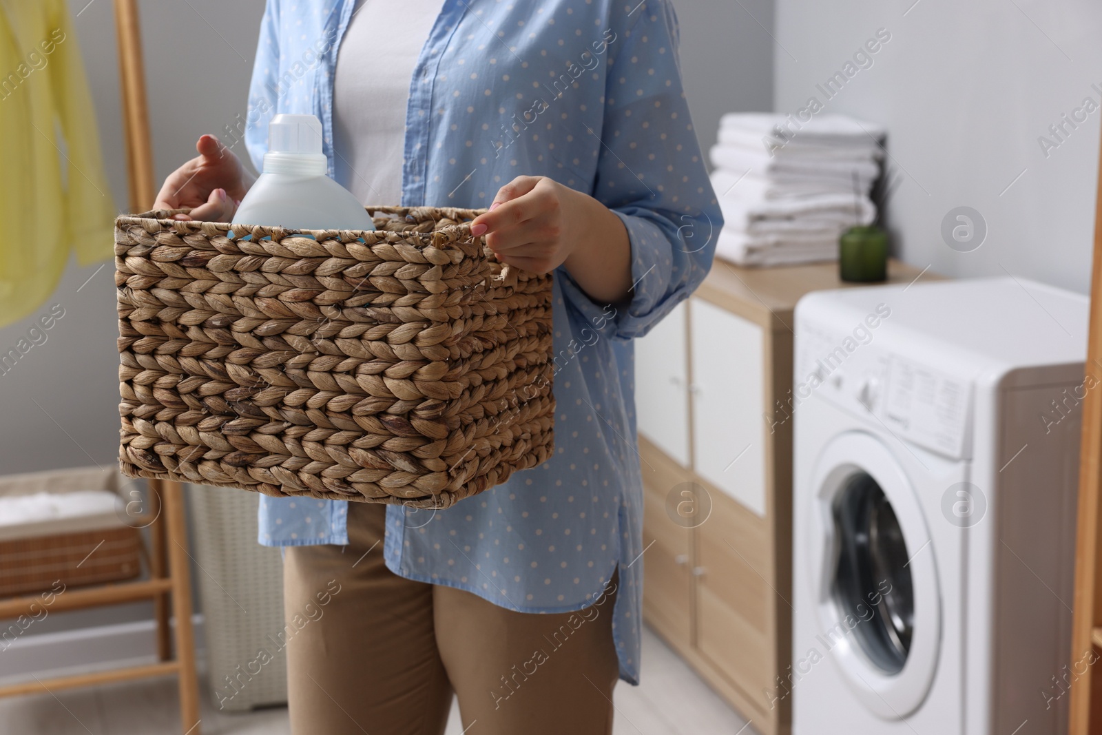 Photo of Woman holding wicker basket with detergent in laundry room, closeup