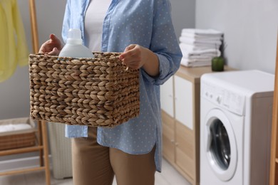 Woman holding wicker basket with detergent in laundry room, closeup