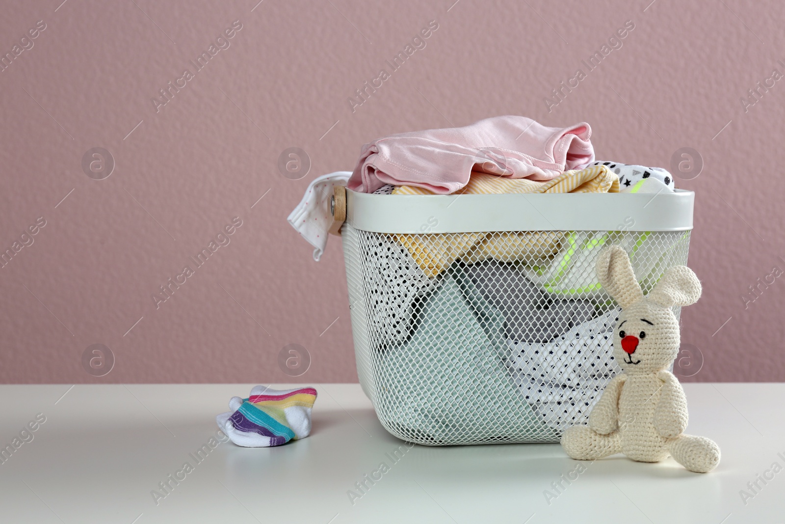 Photo of Laundry basket with different children's clothes and toy on white table. Space for text