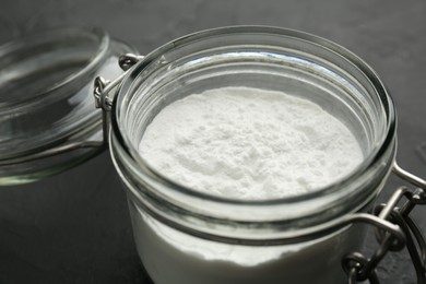 Photo of Baking powder in jar on black table, closeup