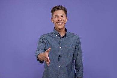 Photo of Happy man welcoming and offering handshake on purple background