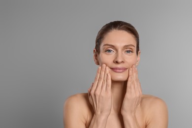 Photo of Woman massaging her face on grey background. Space for text