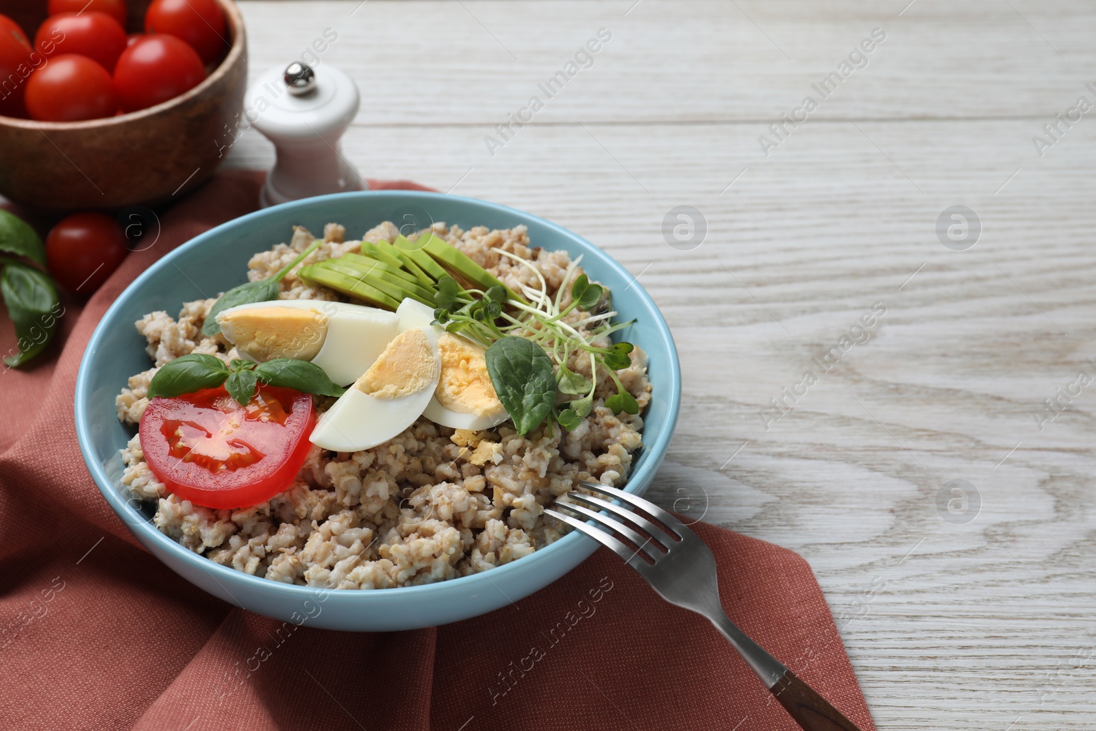 Photo of Delicious boiled oatmeal with egg, tomato and avocado served on light wooden table, space for text