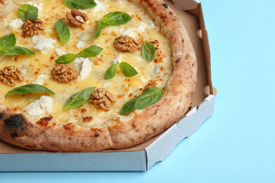 Photo of Delicious cheese pizza with walnuts and basil in takeout box on light blue background, closeup