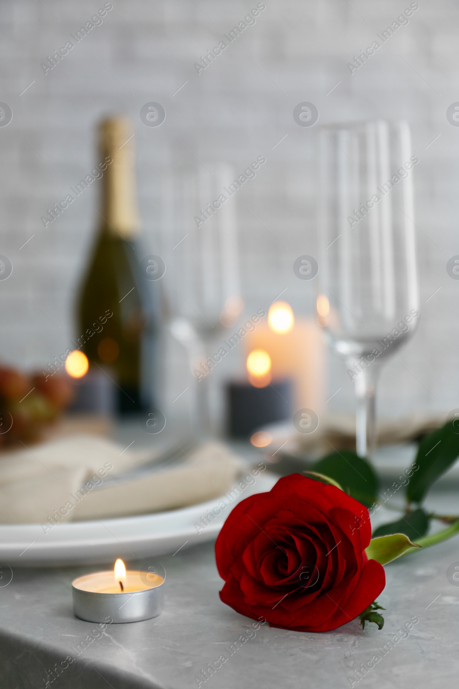 Photo of Burning candle and red rose on grey marble table indoors