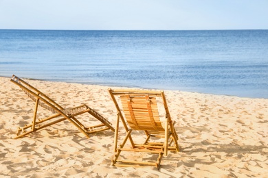 Sandy beach with empty wooden sunbeds on sunny day