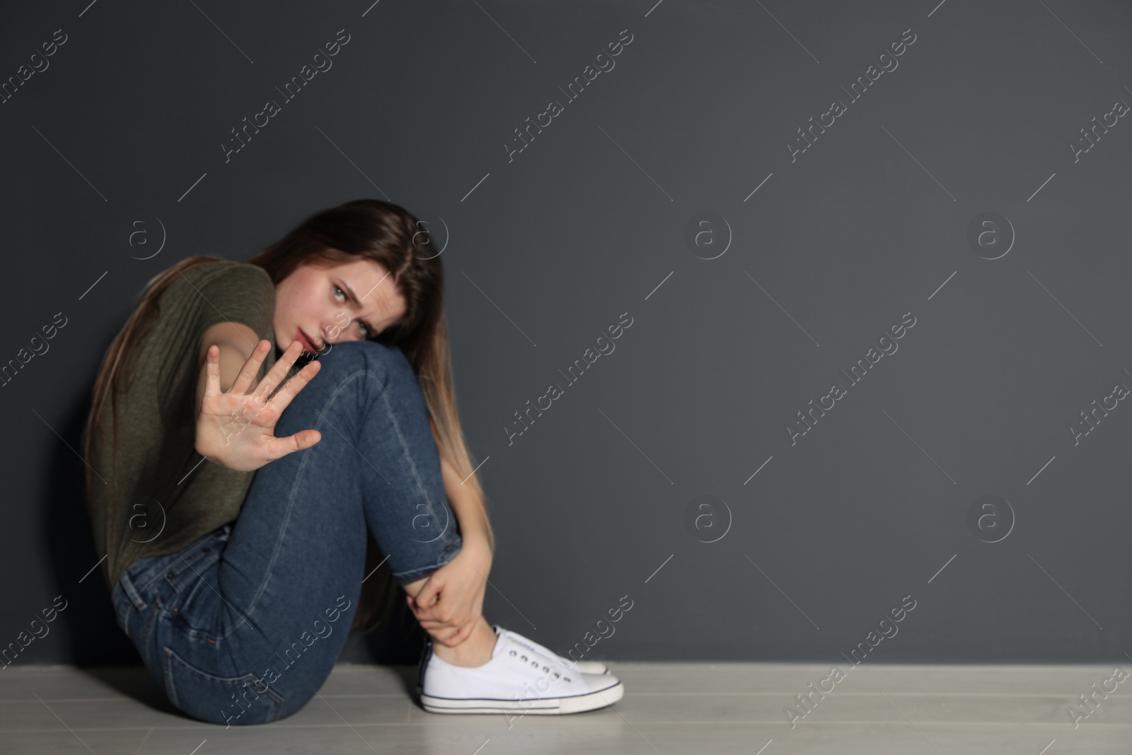 Photo of Young woman making stop gesture while sitting on floor near grey wall. Space for text