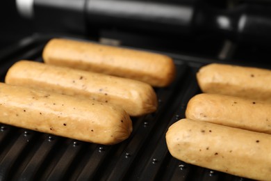 Delicious vegan sausages cooking on electric grill, closeup